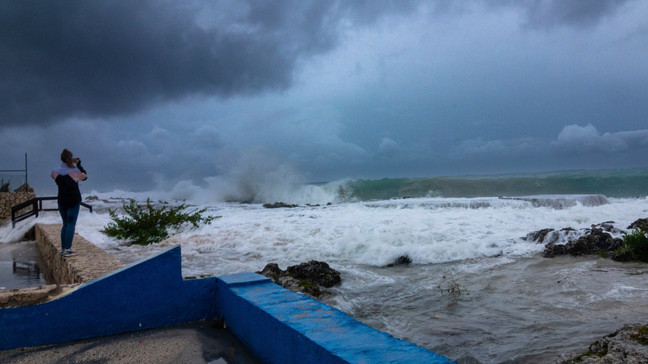 A woman takes photos while waves crash against a seawall as Hurricane Ian passes through George Town, Grand Cayman island, Monday, Sept. 26, 2022. Hurricane Ian is on a track to hit the west coast of Florida as a major hurricane as early as Wednesday. (AP Photo/Kevin Morales)